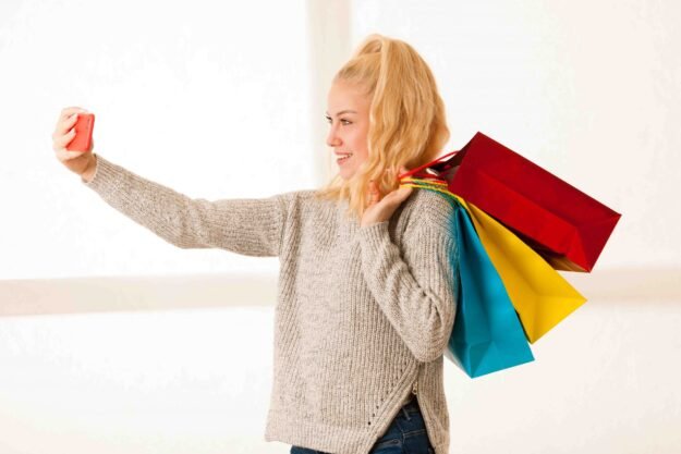 Beautiful blonde woman taking selfie with smart phone after shop